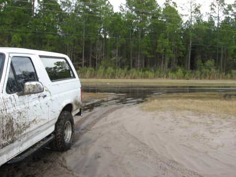 1994 Ford Bronco - White 1994 Ford Bronco with significant mud splatter on its body, seen off-road.