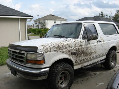 1994 Ford Bronco - A muddy white Ford Bronco is parked in a driveway, showing off its off-road capabilities.