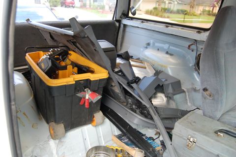 1994 Ford Bronco - The interior of a vehicle is cluttered with car parts and a yellow toolbox, obscuring any identifying features.