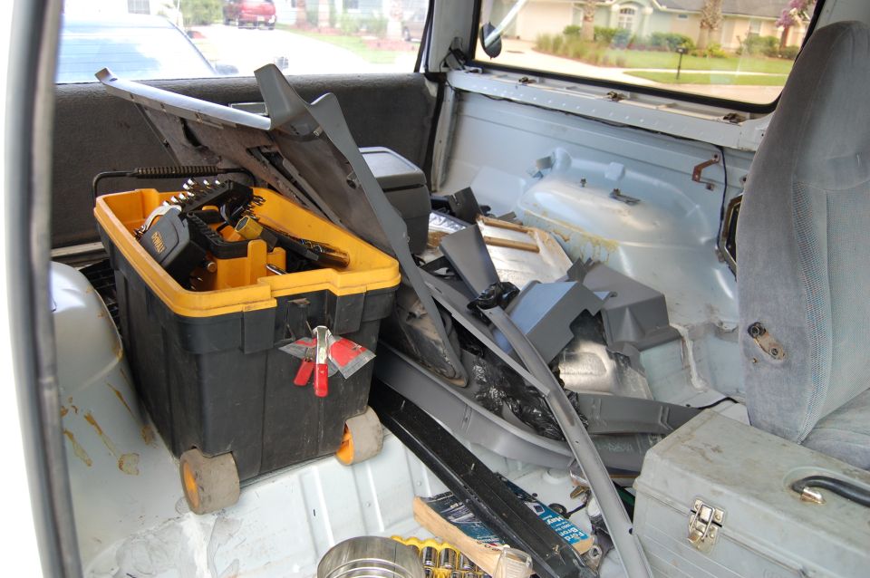 Interior of a vehicle filled with car parts and a yellow toolbox. The seats are gray fabric
