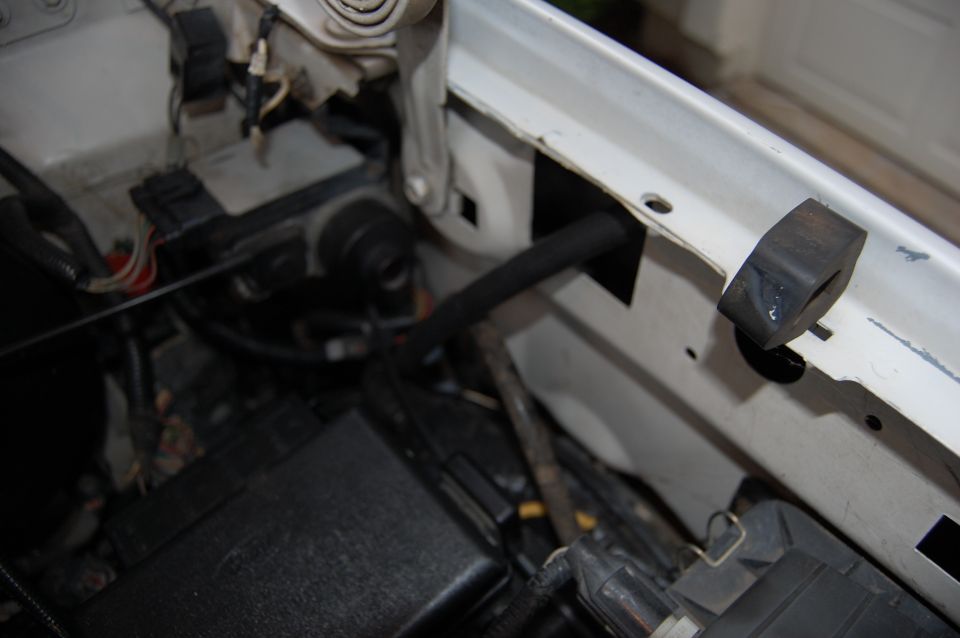 Close-up of engine bay wiring and hoses, with a black rubber stopper visible on the white frame