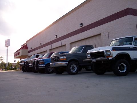 1995 Ford Bronco - Several Ford trucks are parked in a line outside a building, with the closest vehicle being a dark green model from the mid-1990s.