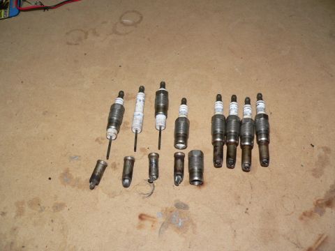 2007 Ford Mustang - Ten spark plugs and four removed tips are laid out on a tan surface with oil stains.