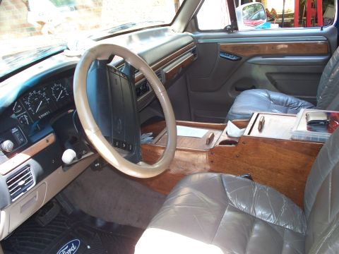 1995 Ford Bronco - The interior of a Ford Bronco shows custom wood paneling and leather seats, with a visible Ford logo on the floor mat.