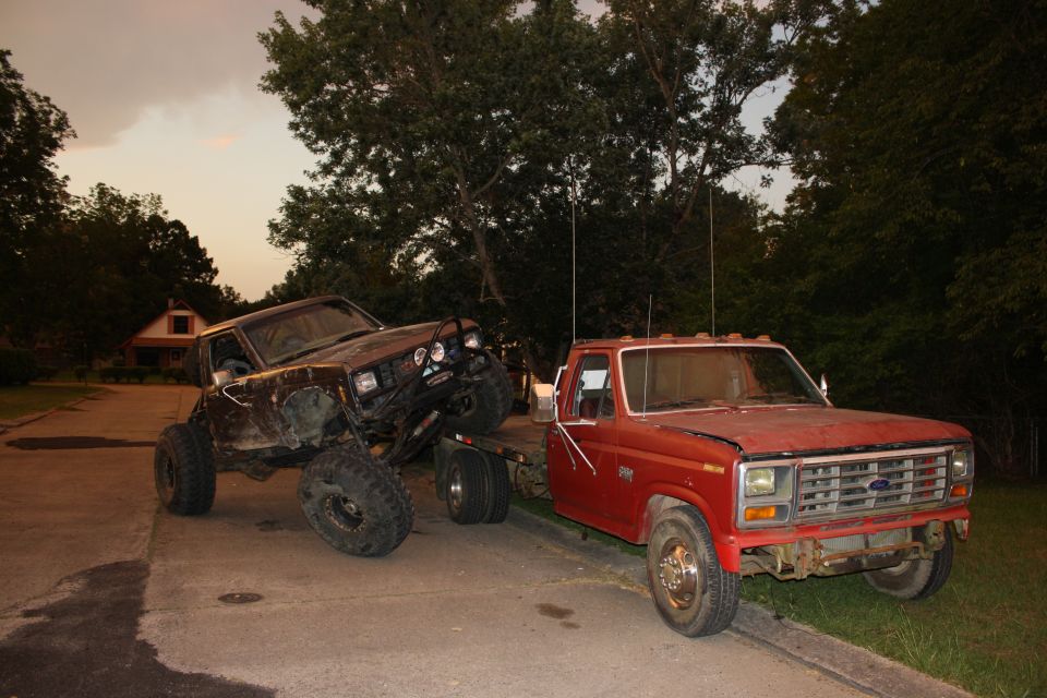 Red Ford F-Series pickup truck towing a heavily modified dark SUV with large tires