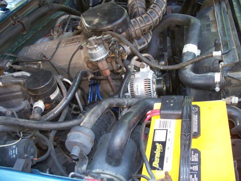 1995 Ford Bronco - Close-up view of an engine bay, a yellow battery and intricate network of hoses and electrical wiring.