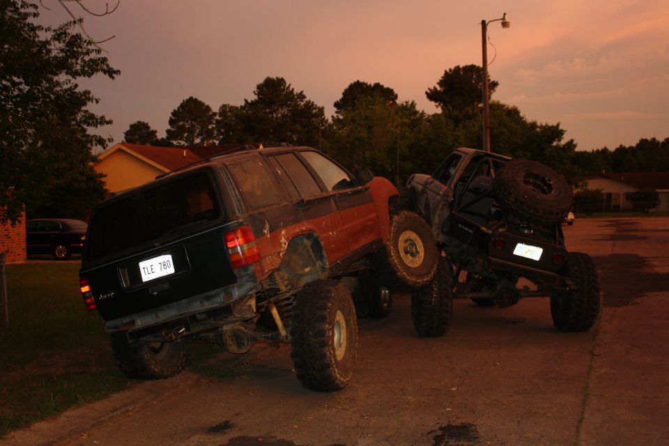 Two modified SUVs, one black and red, the other black with a spare tire on the back, are stuck on a dirt incline