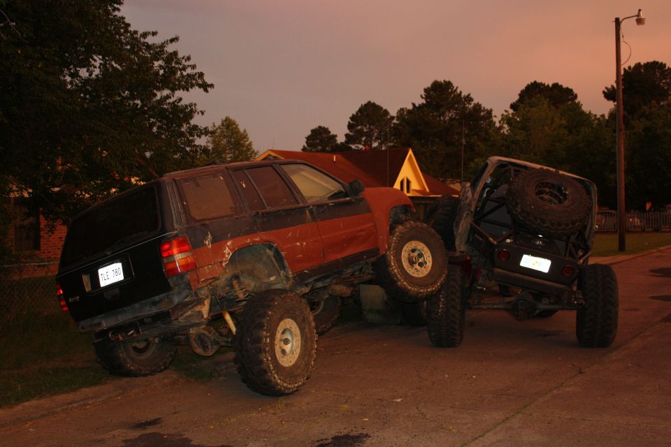 Two SUVs, one red and black, the other black, are stuck on each other on a dirt road