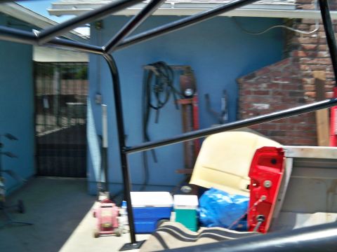 1985 Ford Bronco - Interior view of a truck bed with a roll cage and various parts, including a red door and yellow seat.