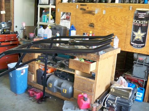 1985 Ford Bronco - Metal frame parts are laid out on a workbench in a cluttered garage setting.