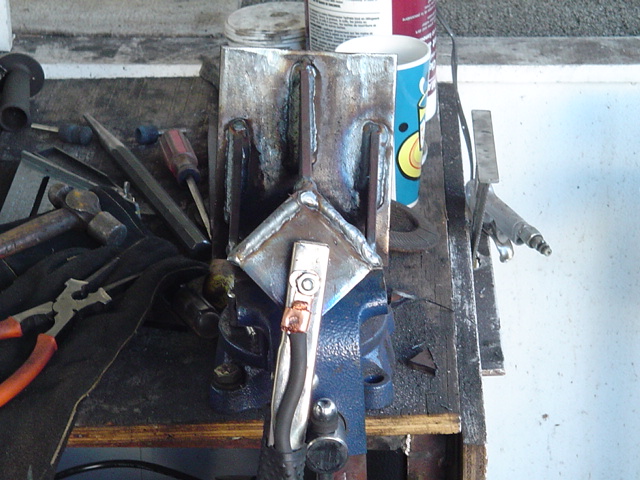 Welded steel bracket held in a blue bench vise on a cluttered workbench