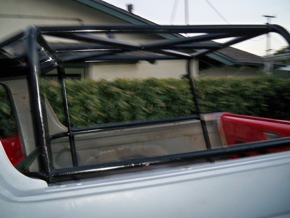 Roll cage structure installed in the bed of a pickup truck, with a red interior visible
