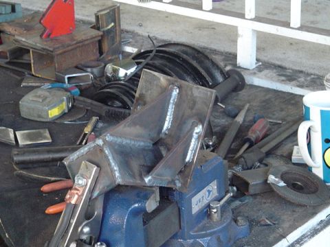 1993 Ford Bronco - A metal bracket is secured in a vise, ready for welding, with various tools scattered around the workbench.