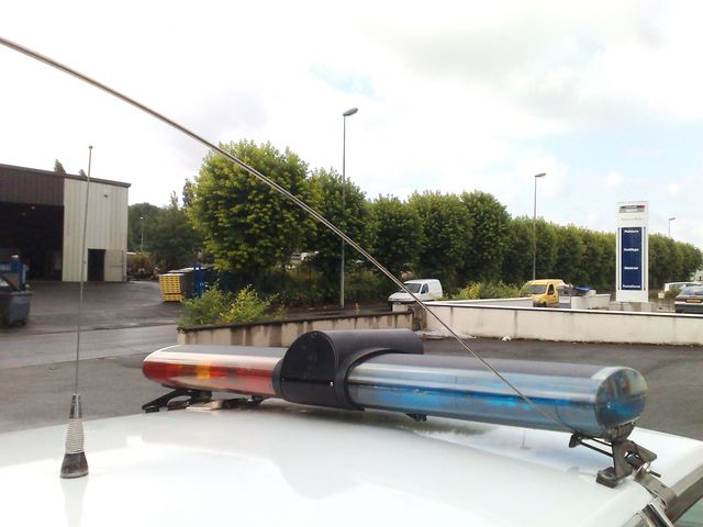 White vehicle roof with a red and blue police light bar and an antenna