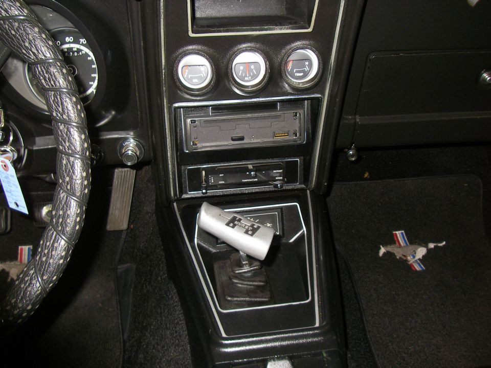 1971 Ford Mustang interior with a black dashboard, three gauges, a car stereo, a floor shifter, and a floor mat with a running horse logo