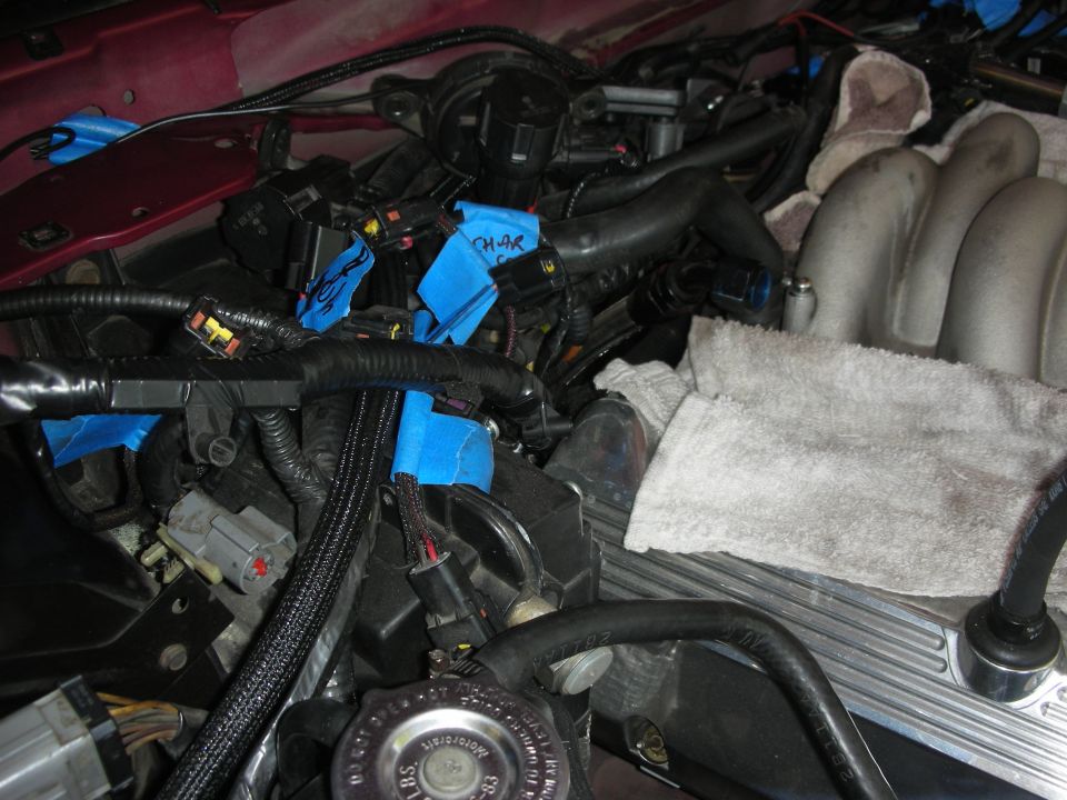 Engine bay wiring harness with blue tape, intake manifold, and a towel