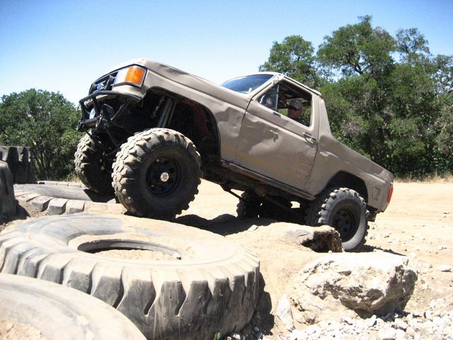 Tan off-road truck with large tires climbing over rocks and tires