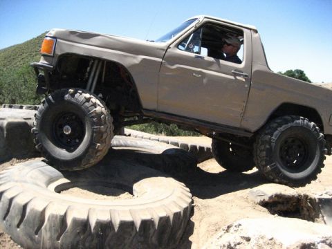 1989 Ford Bronco - A tan off-road SUV is shown navigating a challenging obstacle course made of large tires.