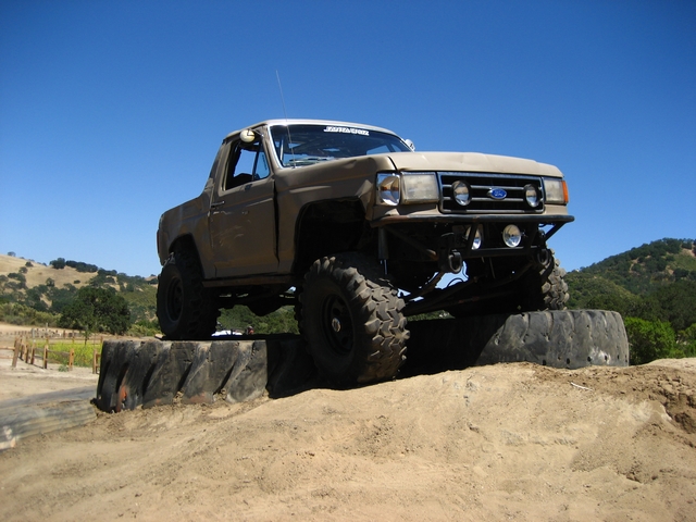 Tan Ford truck with big tires on top of stacked tires, off-road course