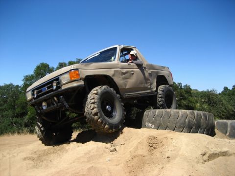 1989 Ford Bronco - A tan 1989 Ford Bronco navigates an off-road obstacle course, demonstrating its capabilities.
