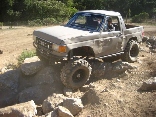 Tan 1989 Ford Bronco climbing rocks on off-road trail