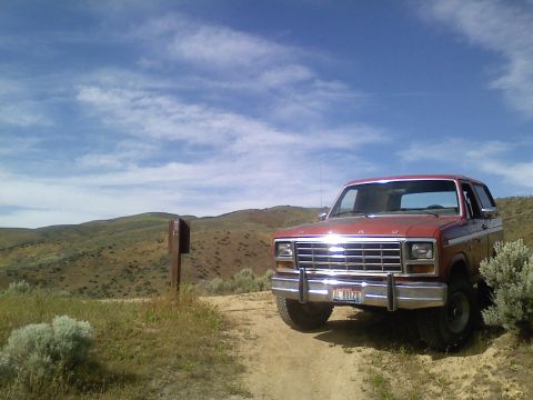 1981 Ford Bronco - 1980s Ford Bronco parked on a dirt road in a hilly, arid landscape under a cloudy blue sky.