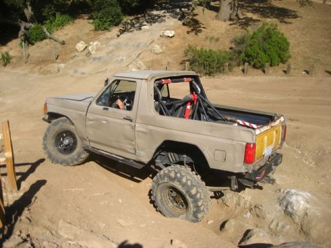 1989 Ford Bronco - A tan Ford Bronco navigates a challenging off-road course, demonstrating its capabilities.