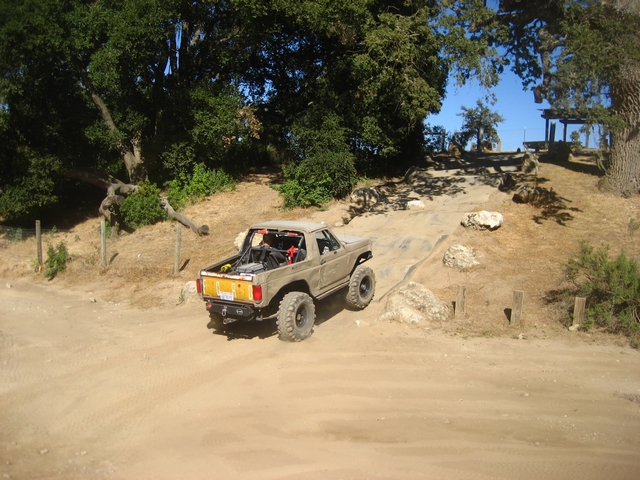 Tan Ford Bronco off-roading on a dirt path with large tires and a roll cage