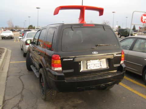 1996 Ford Bronco - This black SUV has a prominent red spoiler mounted on its roof, and is parked in a lot with other vehicles.