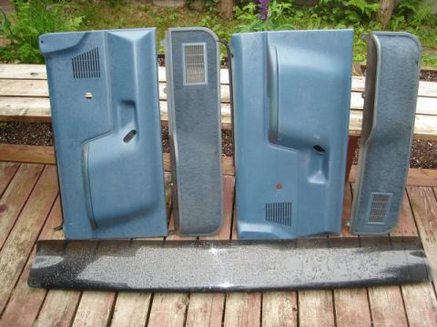 1989 Ford Bronco - Several blue interior door panels and a piece of trim are displayed on a weathered wooden surface outdoors.