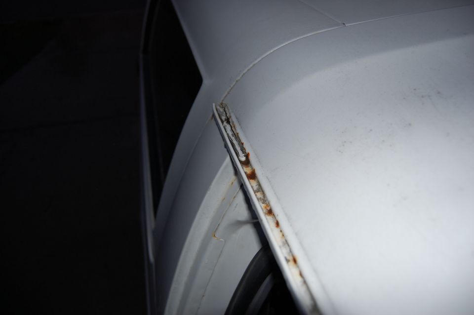 Close-up of a rusted seam on the white body of a vehicle, likely a door or roof edge