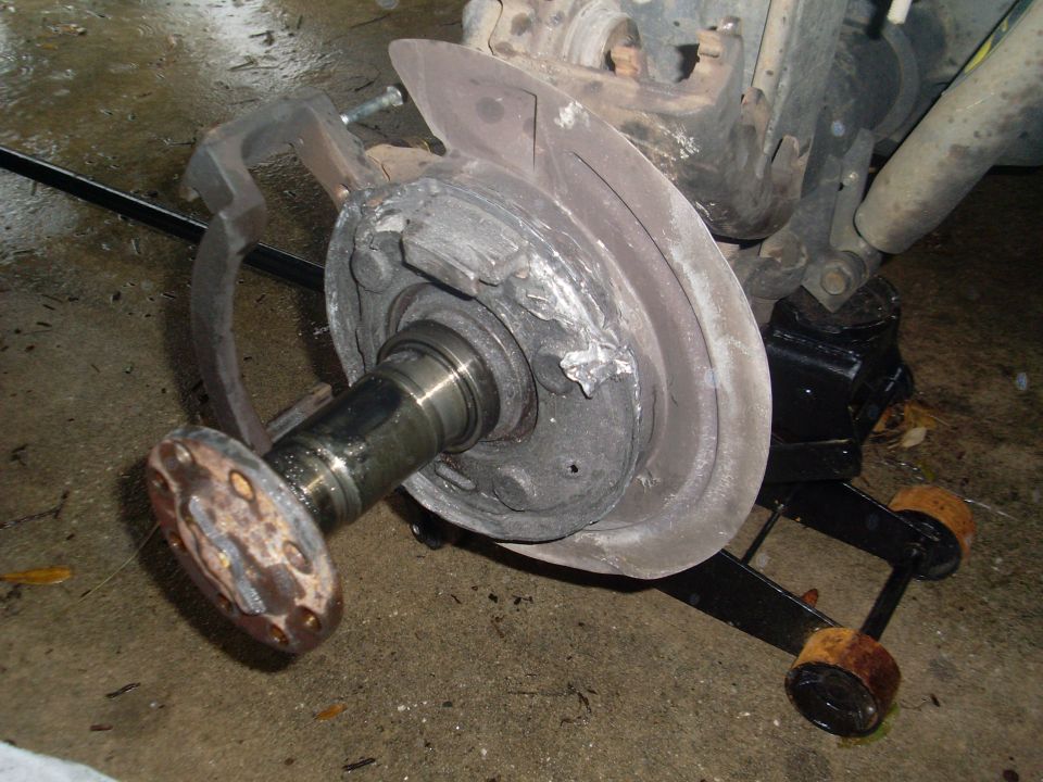 Vehicle axle and brake assembly on a jack. Shows rotor, caliper, and hub