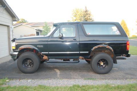 1994 Ford Bronco - Side view of a black 1994 Ford Bronco with visible rust damage on the body.