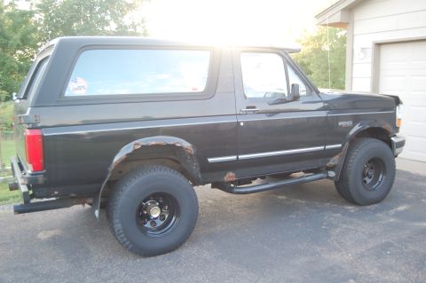 1994 Ford Bronco - This 1994 Ford Bronco is shown from the side, parked in front of a garage with trees in the background.