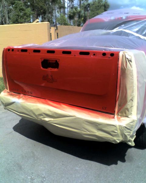 1993 Ford C-350 (Centurion Conversions) - A red pickup truck tailgate, identified as a Silverado 1500 LT, is covered in plastic sheeting during a paint job.