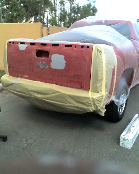 1993 Ford C-350 (Centurion Conversions) - Rear view of a red pickup truck tailgate, prepped for paint with protective coverings and tape.