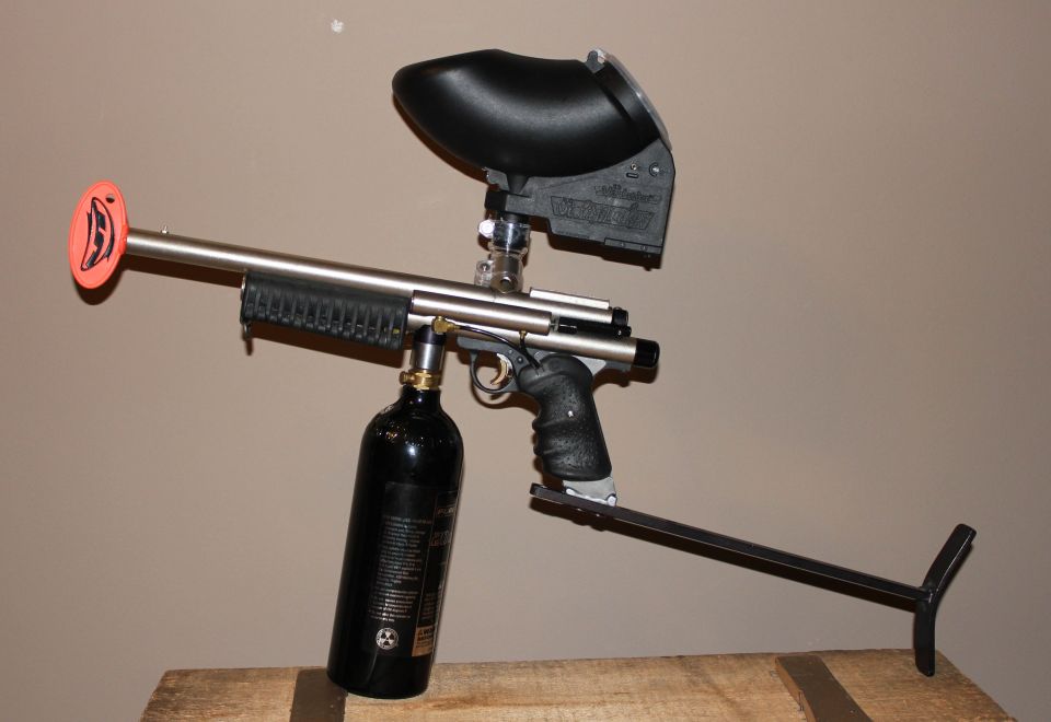 Pump paintball marker with stainless barrel, black hopper and CO2 tank on wood bench