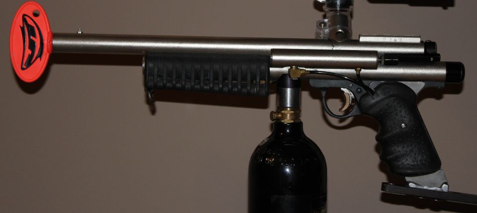 Stainless pump paintball marker with black pump grip, CO2 bottle and orange barrel plug