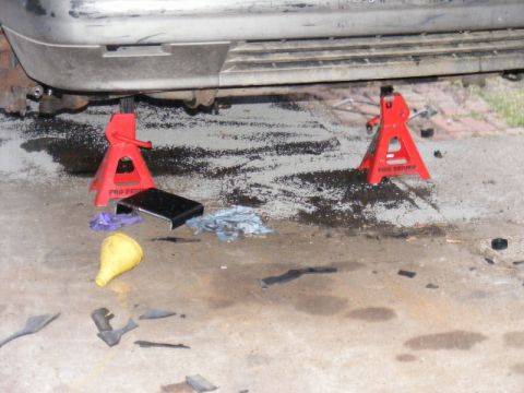 1989 Ford Escort - A vehicle is raised on jack stands, with a yellow funnel and tools scattered on the ground below.