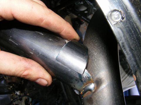 1989 Ford Escort - Close-up of a hand working on a damaged exhaust pipe, showing a section being welded.