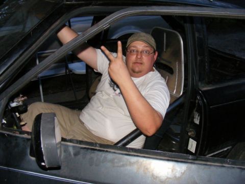 1989 Ford Escort - Man sits inside a car, giving a peace sign.