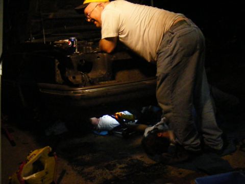 1989 Ford Escort - Two people are working on the engine of a car at night, with one person looking into the engine bay and another underneath.