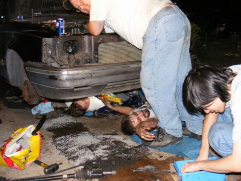 1989 Ford Escort - Mechanics are working on the engine of a car, with tools and parts scattered around.