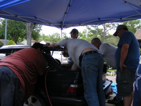 1989 Ford Escort - Several individuals are gathered around the rear of a car, seemingly performing maintenance or modifications.