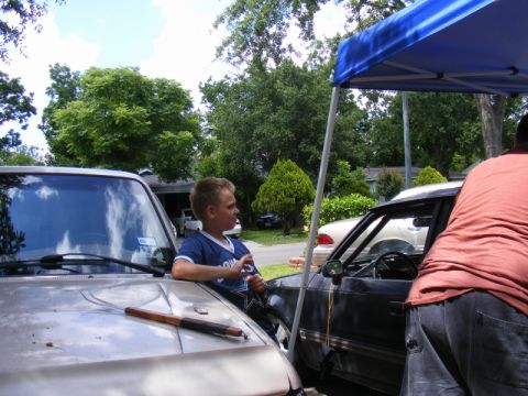 1989 Ford Escort - A boy stands between two cars, one tan and one black, under a blue canopy.