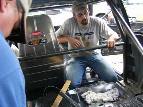 1989 Ford Escort - Mechanics work on the interior of a car, which features Kirkey racing seats and a roll cage.