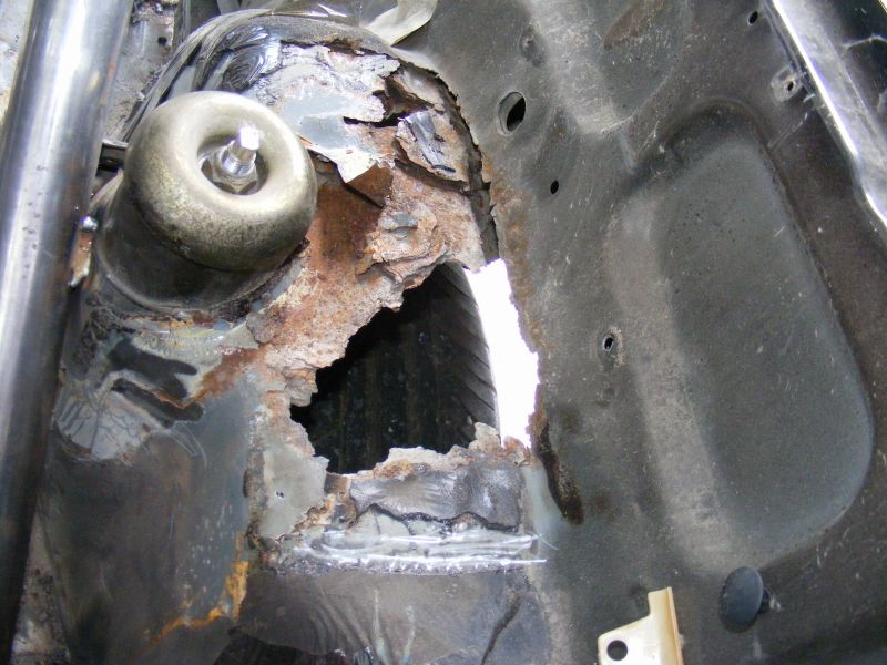 Heavily rusted car chassis with a large hole showing a tire and suspension components