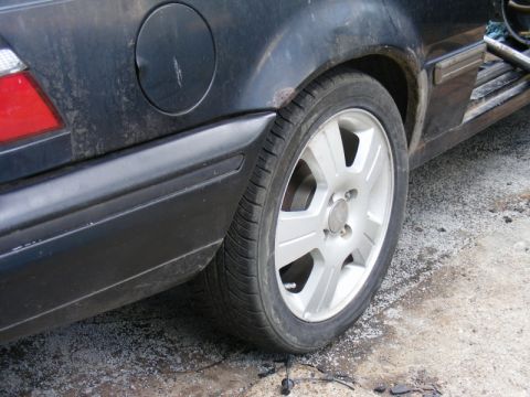 1989 Ford Escort - The rear quarter panel and wheel of a dark-colored vehicle show signs of wear and rust.