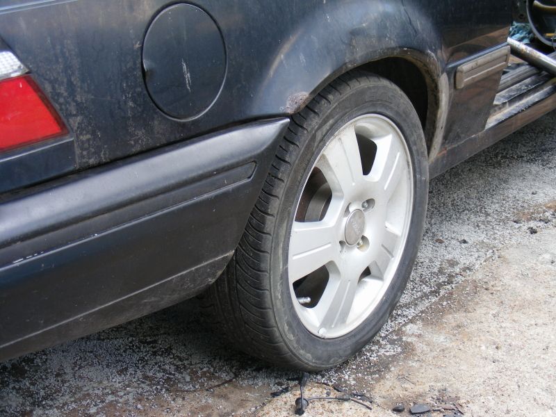 Black car's rear wheel and fender with rust visible