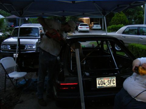 1989 Ford Escort - A person works on a black car with a roll cage, visible in the rear view.